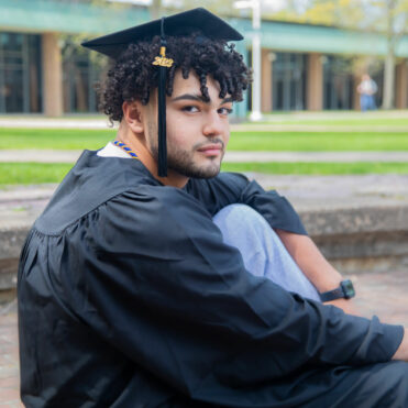 Christian Ruiz sits outside wearing graduation cap and gown